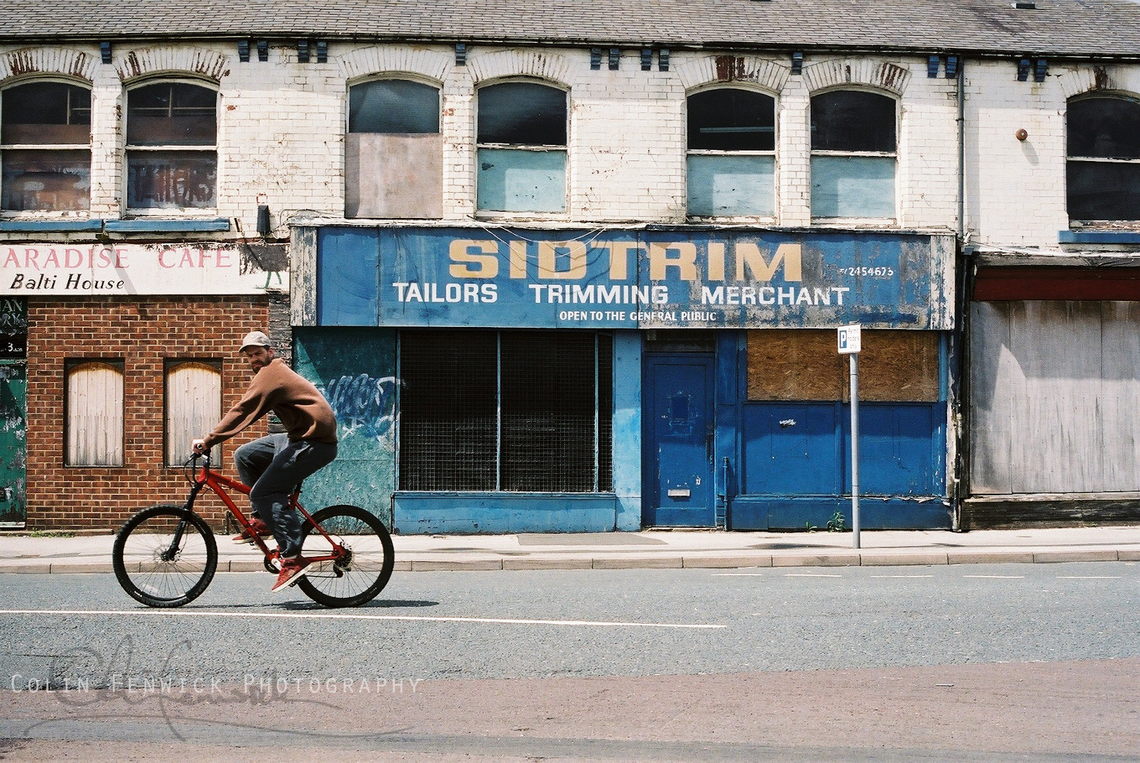 man riding bike past derelict building