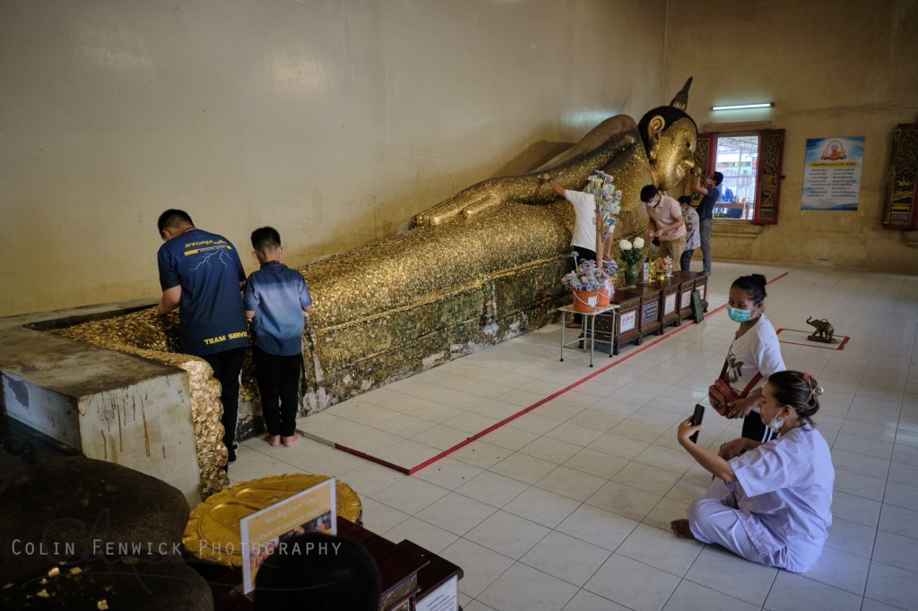 People attach gold leaf to a leaning buddha statue