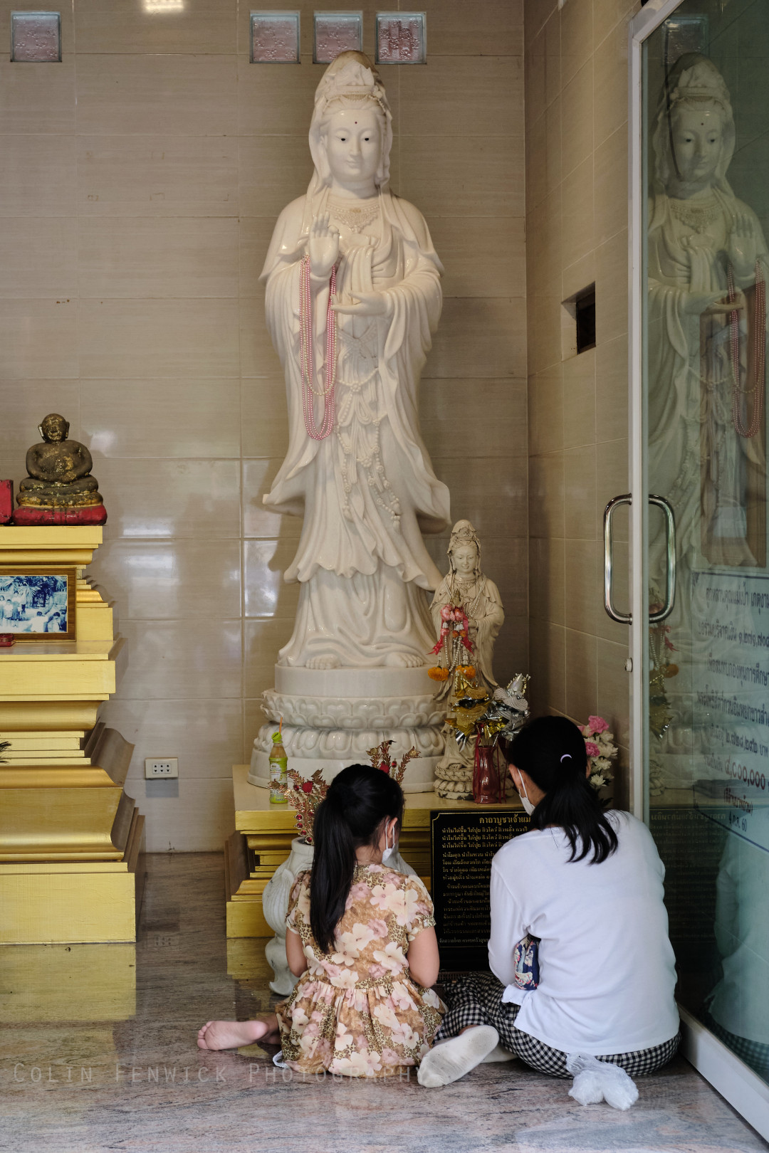 Mother and daughter pray in front of a statue of Guanyin